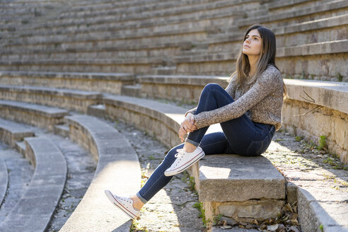 Junge Frau sitzt auf einer Treppe im Freien und schaut sich um - AFVF02436