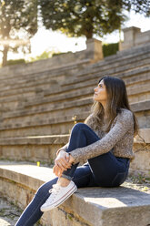 Junge Frau sitzt auf einer Treppe im Freien und schaut sich um - AFVF02437
