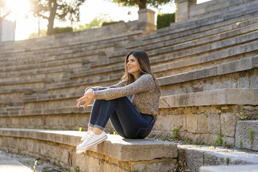 Happy young woman sitting on stairs outdoors - AFVF02439