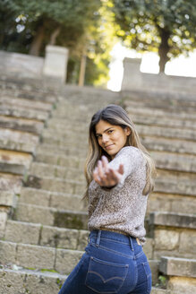 Porträt einer jungen Frau auf einer Treppe, die ihre Hand ausstreckt - AFVF02445