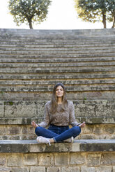 Young woman sitting outdoors on stairs doing yoga - AFVF02447