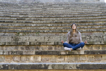 Young woman sitting outdoors on stairs doing yoga - AFVF02448