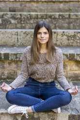 Young woman sitting outdoors on stairs doing yoga - AFVF02449