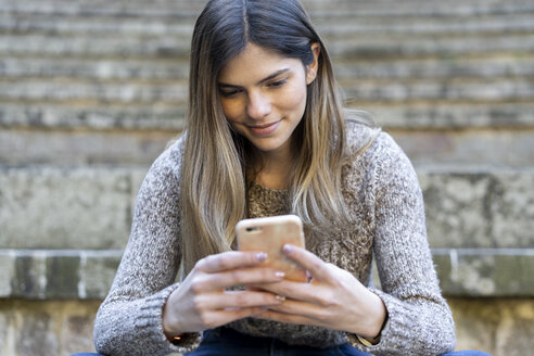 Junge Frau sitzt auf einer Treppe im Freien und benutzt ein Mobiltelefon - AFVF02450
