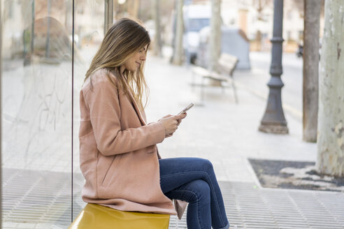 Junge Frau mit Mobiltelefon an der Bushaltestelle - AFVF02465