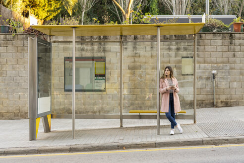Young woman with cell phone waiting at bus stop - AFVF02466