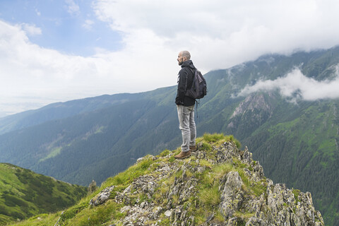 Mann steht auf einem Hügel und betrachtet die Landschaft in den Karpaten, Rumänien, lizenzfreies Stockfoto