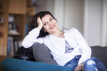 Portrait of smiling young woman sitting on couch at home relaxing - SGF02233