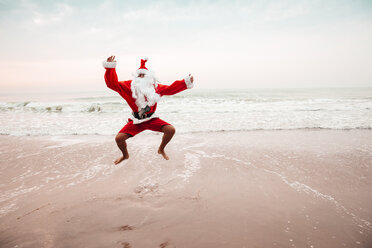 Thailand, man dressed up as Santa Claus jumping in the air on the beach - HMEF00218