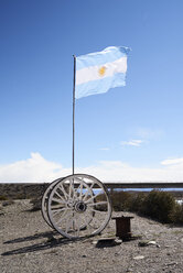 Argentinien, Patagonien, argentinische Flagge auf Holzrädern gegen blauen Himmel - IGGF00787