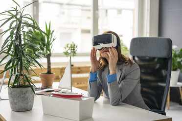 Businesswoman sitting at desk with a ship model, looking through VR glasses - MOEF01993
