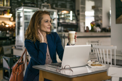 Geschäftsfrau, die in einem Café sitzt, zu Mittag isst und am Laptop arbeitet, lizenzfreies Stockfoto