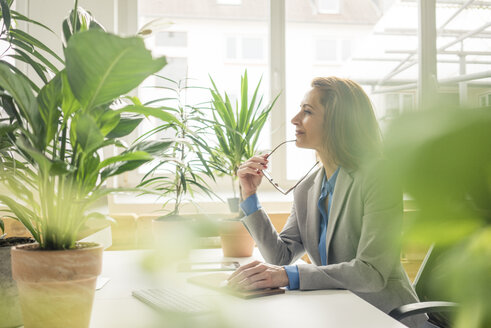 Reife Geschäftsfrau, die in einem nachhaltigen Büro arbeitet, mit Pflanzen auf ihrem Schreibtisch - MOEF02026