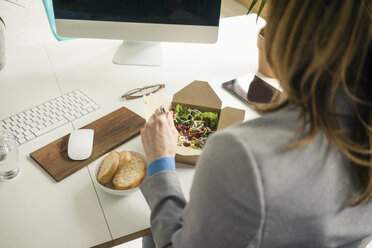 Frau isst Salat zum Mittagessen an ihrem Schreibtisch - MOEF02028