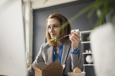 Businesswoman sitting in office, working on PC, eating lunch - MOEF02029