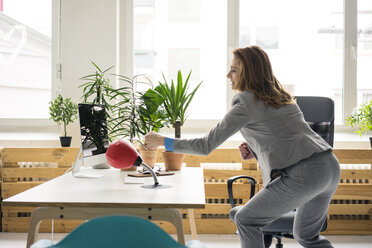 Geschäftsfrau beim Boxen eines Punchingballs in ihrem Büro - MOEF02035