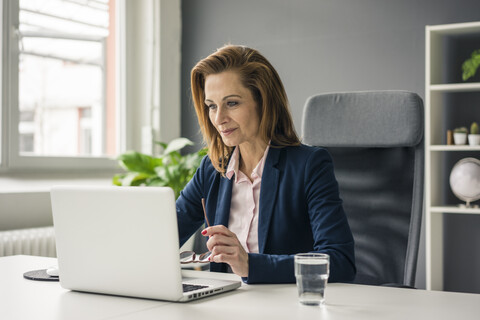 Geschäftsfrau sitzt im Büro und arbeitet am Laptop, lizenzfreies Stockfoto