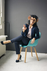 Businesswoman sitting on chair, wearing monkey mask, gesturing - MOEF02067
