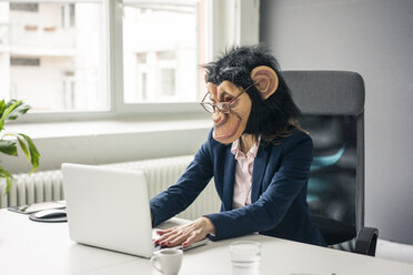 Geschäftsfrau mit Schimpansenmaske arbeitet im Büro und benutzt einen Laptop - MOEF02068