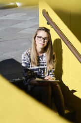 Portrait of blond student with notebook sitting on stairs outdoors - IGGF00796