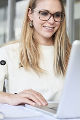 Porträt einer lächelnden jungen Geschäftsfrau, die an einem Laptop arbeitet - IGGF00801