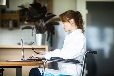 Junger Arzt im Rollstuhl arbeitet am Laptop - SGF02244