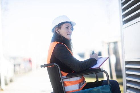 Junger Techniker mit Schutzhelm und Schutzweste im Rollstuhl bei der Arbeit im Freien - SGF02251