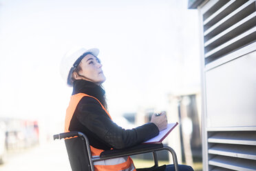 Young technician with safety helmet and vest in wheelchair working outdoors - SGF02252