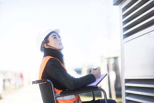 Junger Techniker mit Schutzhelm und Schutzweste im Rollstuhl bei der Arbeit im Freien - SGF02252