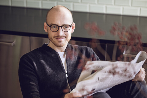 Mann sitzt in der Küche und liest Zeitung, lizenzfreies Stockfoto