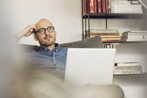 Mann sitzt auf Couch, benutzt Laptop, lizenzfreies Stockfoto