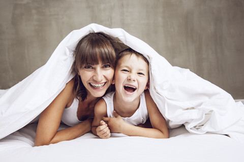 Mutter und Sohn kuscheln unter der Decke, lachend, lizenzfreies Stockfoto