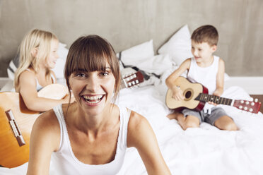 happy mother with children playing guitar in bed - MCF00054