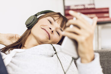 Woman lying couch, listening music with headphones - MCF00059
