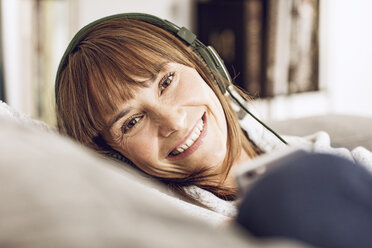 Woman lying couch, listening music with headphones - MCF00060