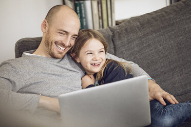 Vater und Tochter sitzen auf der Couch und benutzen einen Laptop - MCF00098