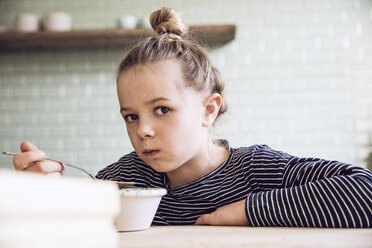 Sceptical girl sitting in kitchen, eating granola - MCF00101