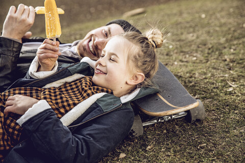 Vater und Tochter ruhen sich auf dem Skateboard aus und essen Eiscreme, lizenzfreies Stockfoto