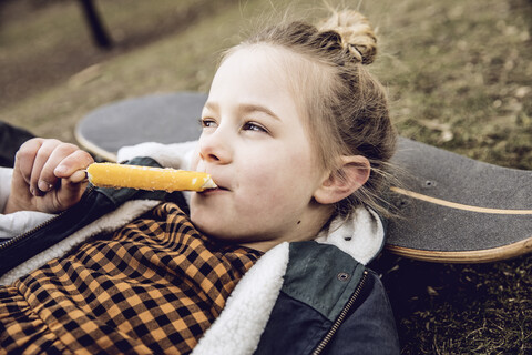 Kleines Mädchen isst ein Eis und stützt den Kopf auf ein Skateboard, lizenzfreies Stockfoto