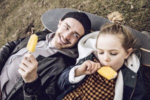 Vater und Tochter ruhen sich auf dem Skateboard aus und essen Eiscreme - MCF00104