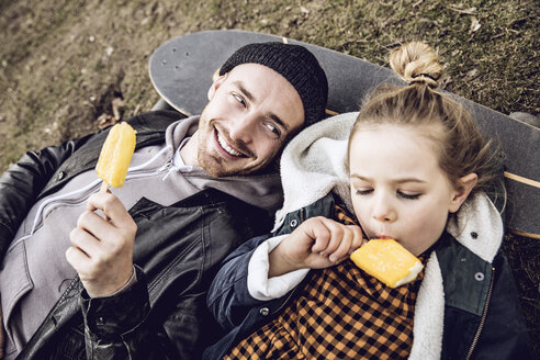 Father and daughter resting on skateboard, eating ice cream - MCF00104