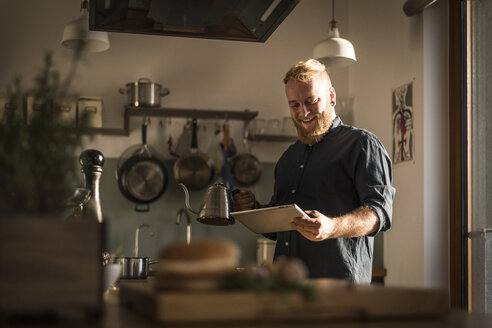 Young man standing in kitchen, reading online recipe on his digital tablet - MJRF00001