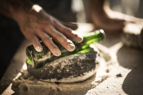 Man preparing black burger buns in kitchen, rolling dough with a bottle - MJRF00019