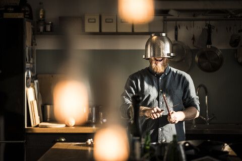 Mann schärft Küche, trägt Sieb als Helm, lizenzfreies Stockfoto