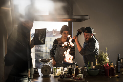 Freunde flambieren Essen in einer Pfanne, wobei eine große Flamme entsteht, während ein Freund filmt - MJRF00058
