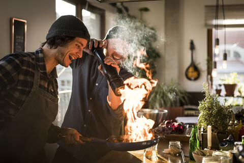 Freunde flambieren Essen in einer Pfanne, wodurch eine große Flamme entsteht, lizenzfreies Stockfoto