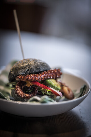 Schwarzer Burger mit gebratenem Oktopus und Gemüse, lizenzfreies Stockfoto