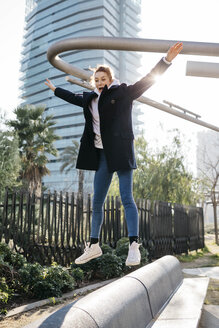 Junge Frau balanciert und springt auf einer Stadtbank - JRFF02676
