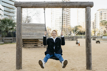 Portrait of happy young woman on a swing on playground - JRFF02679