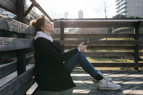 Junge Frau, die sich im Freien ausruht und ein Mobiltelefon hält - JRFF02682
